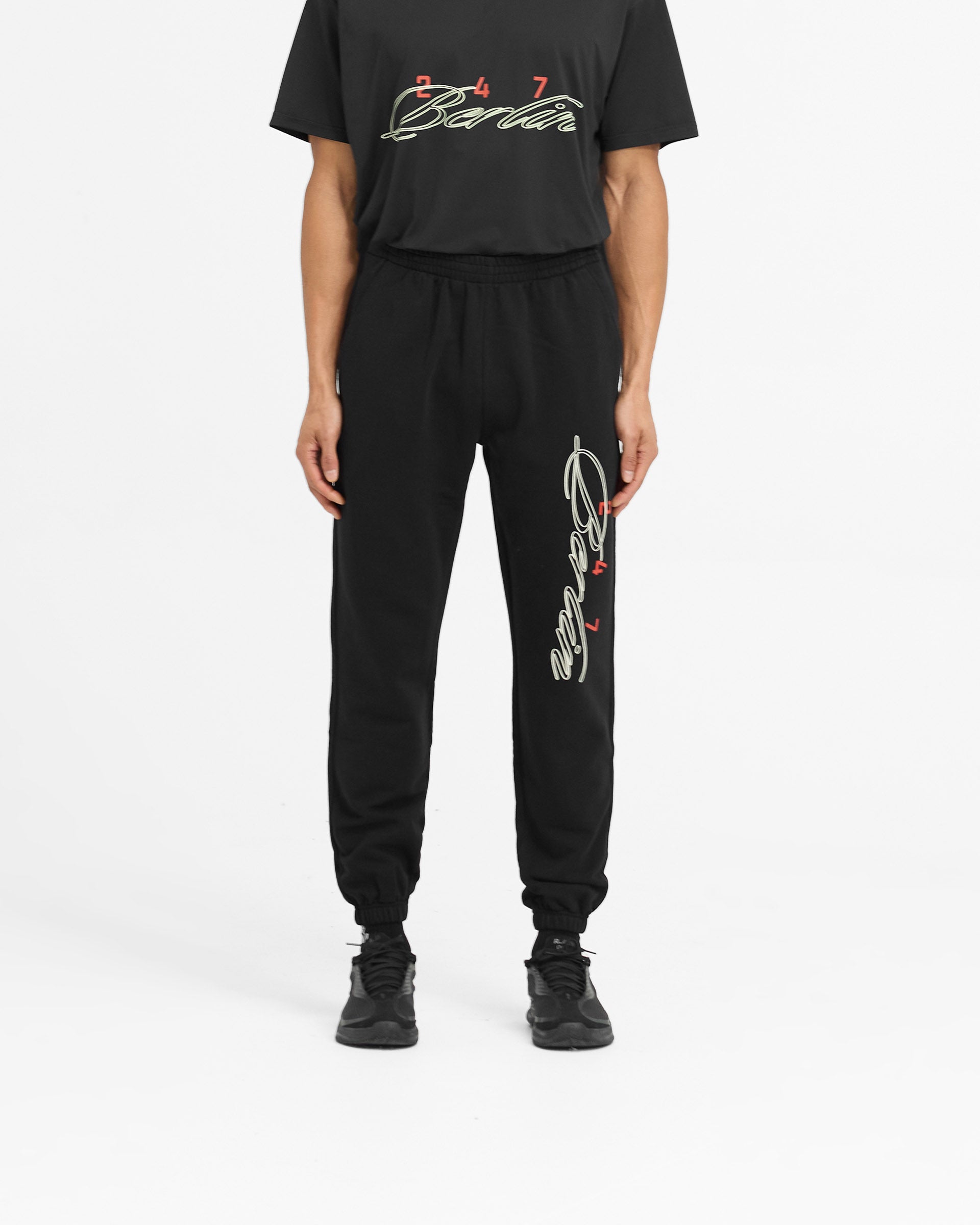 Man wearing black sweatpants with Berlin script on a plain white background | 247 Berlin Sweatpant in Black | Joggers with elasticated cuffs and internal drawcord | 247 Pants | Represent Clo