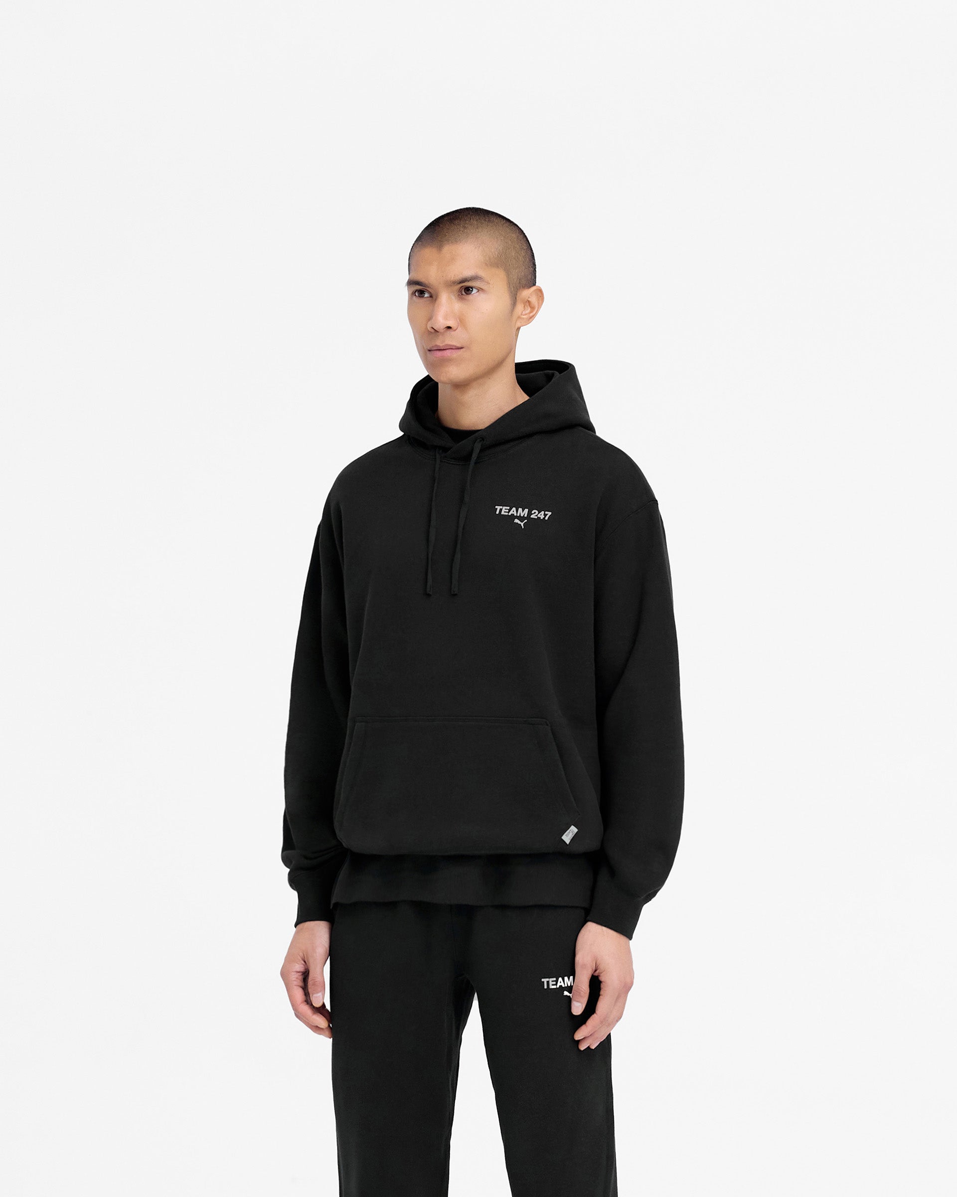 Man wearing a black hoodie on a plain white background | 247 X Puma Hoodie in Black | Relaxed fit hoodie with 3D silicon branding and adjustable drawcord | 247 Hoodies | Represent Clo